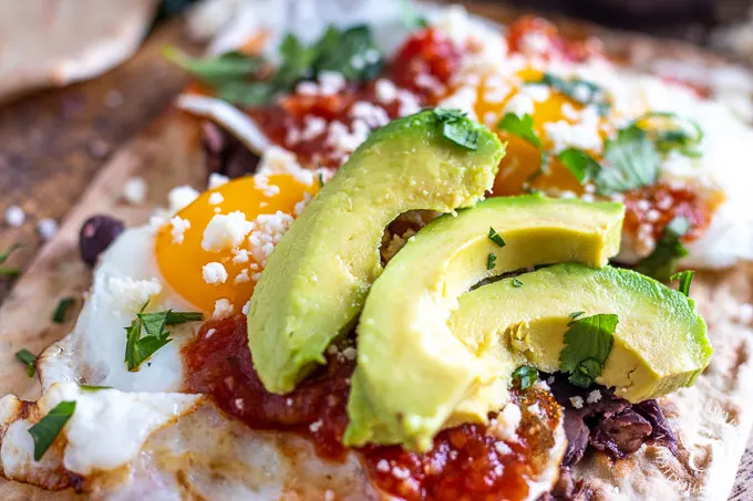 Flatbread Huevos Rancheros with sliced avocados 